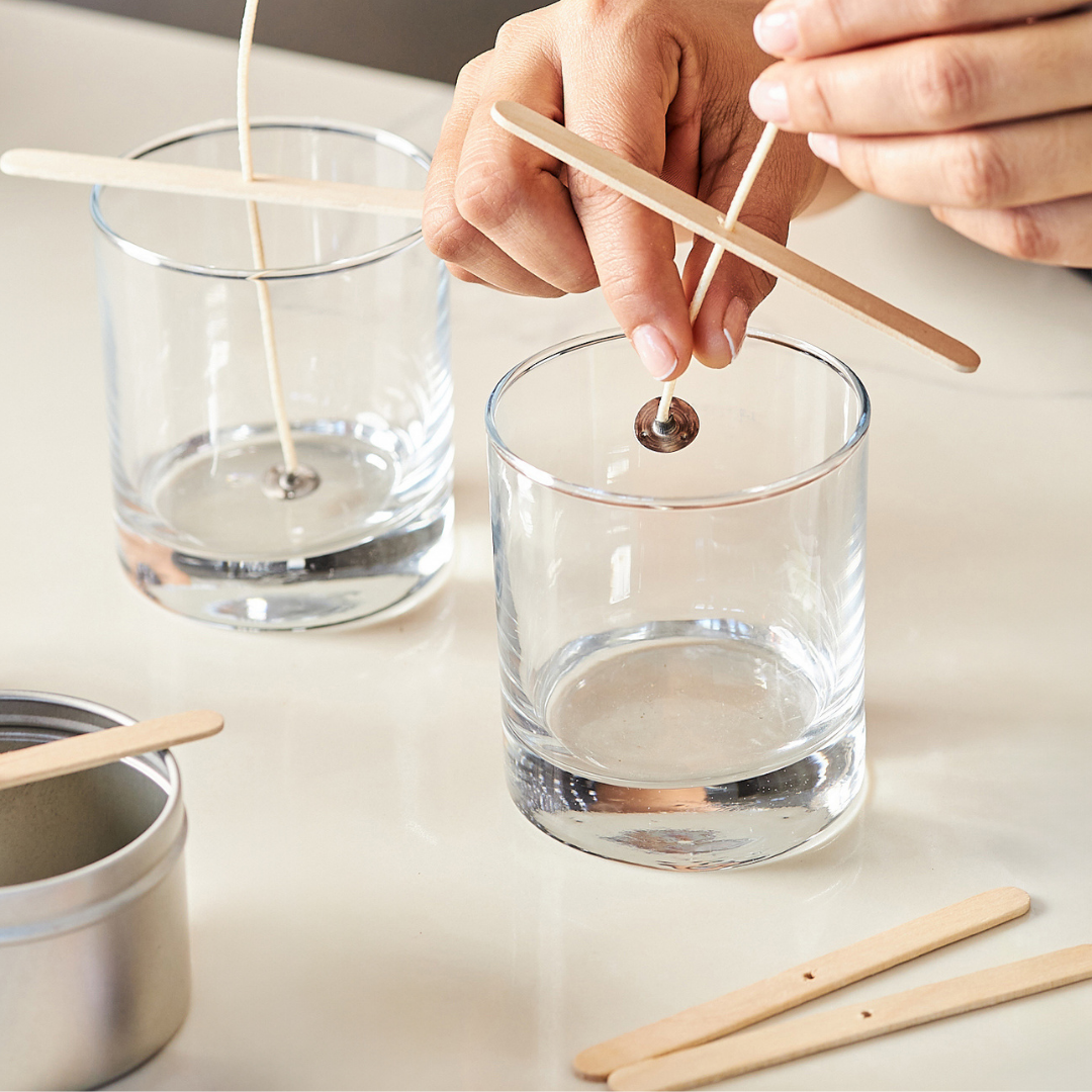 Hands placing pre-tabbed wicks in clear glass jars
