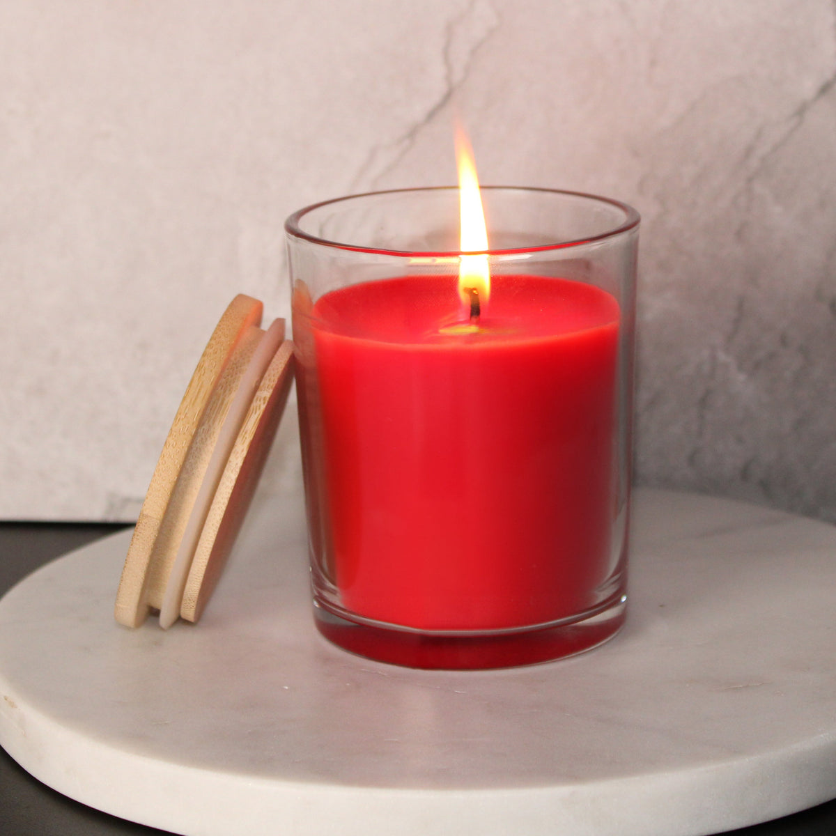 Lit red candle in a 7 oz clear glass jar