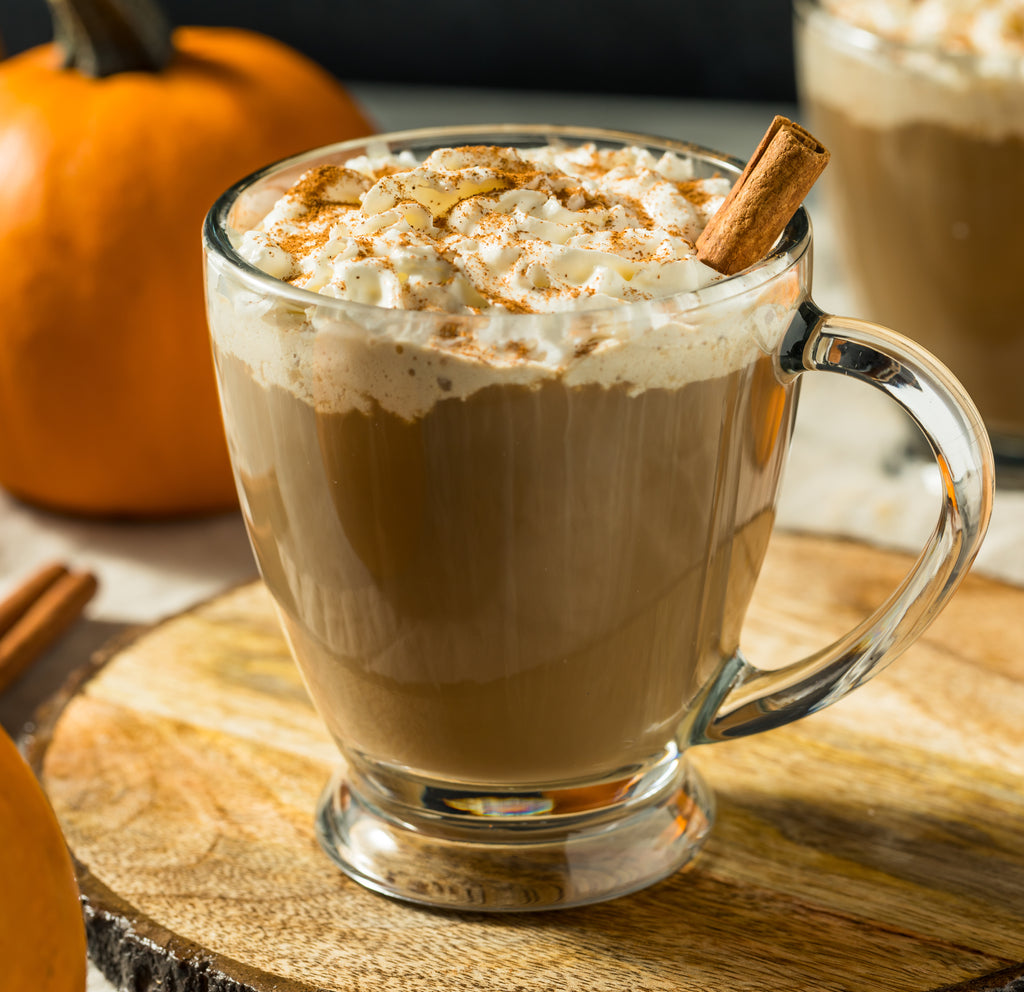 Pumpkin latte topped with whipped cream next to a small pumpkin