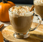 Pumpkin latte topped with whipped cream next to a small pumpkin