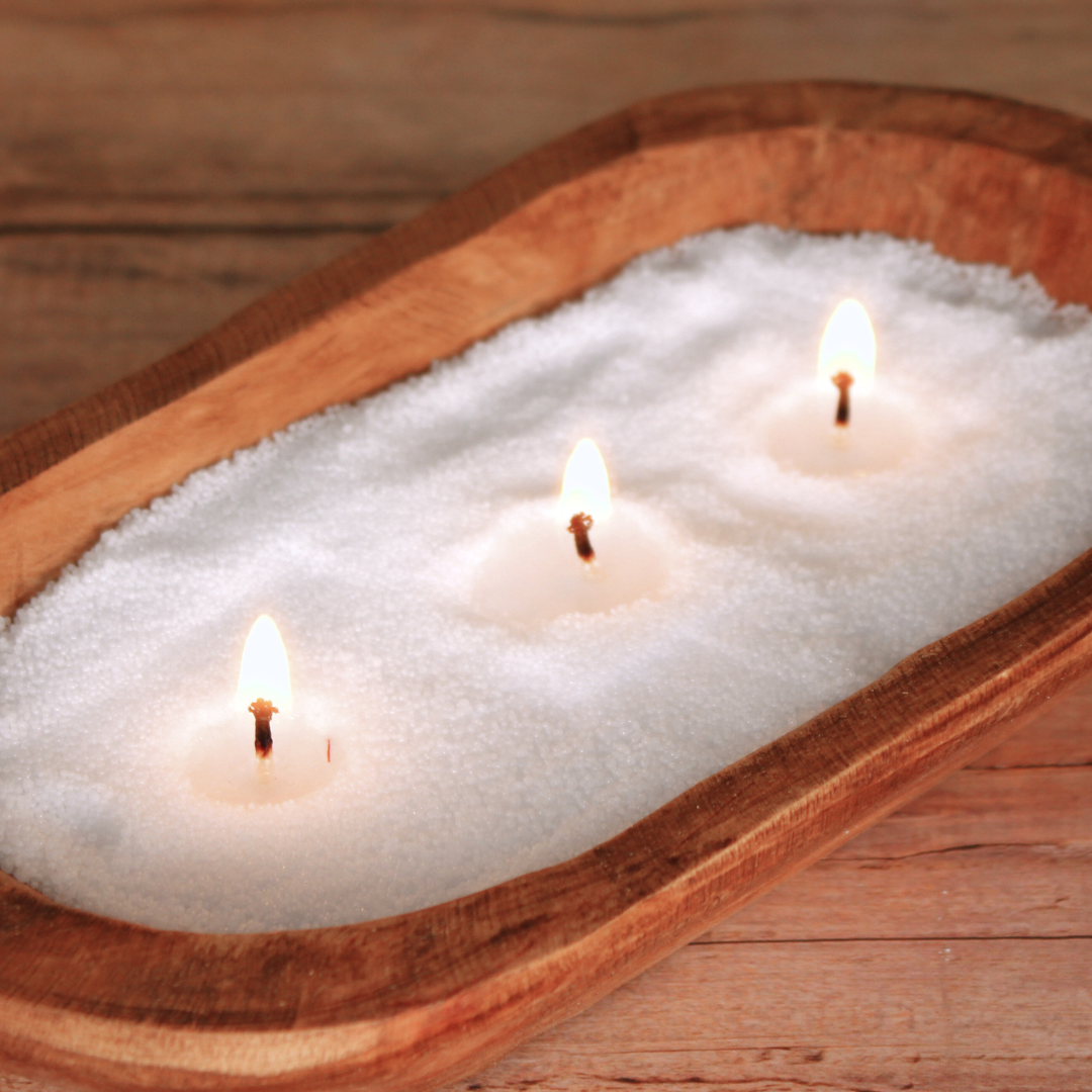 White pearled candle wax with three lit wicks in a wooden bowl