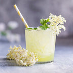 Elderflower lemonade in a glass with elderflower blossoms and a straw