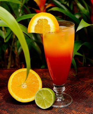 multihued tropical drink in tall glass with exotic plants in background